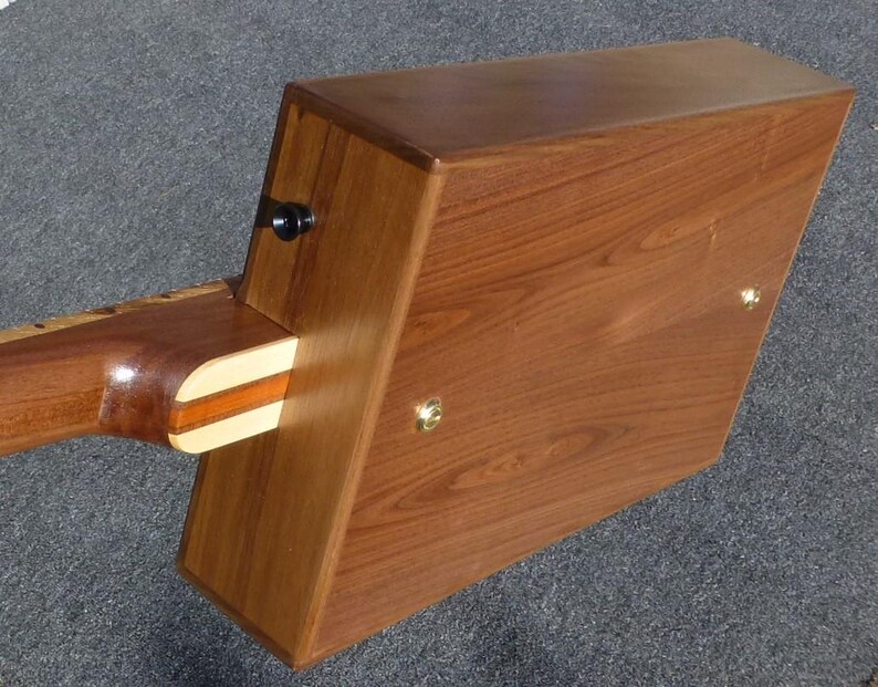 May include: A wooden box with a guitar neck attached to the side. The box is made of dark wood with a light wood trim. The guitar neck is made of light wood with a dark wood fretboard.