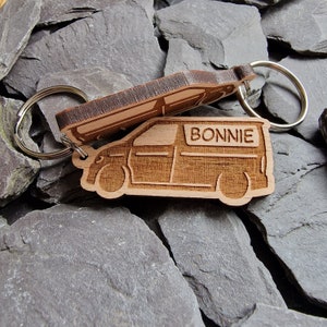 May include: Wooden keychain shaped like a van with the name "BONNIE" engraved on the side. The keychain is attached to a silver metal ring.