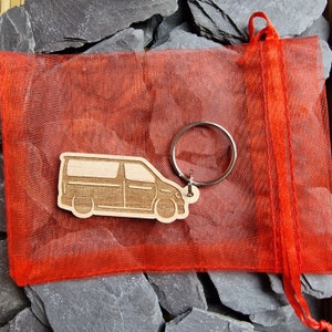 May include: A wooden keychain shaped like a van, with a silver key ring. The keychain is in a red mesh bag.