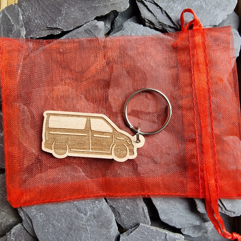 May include: A wooden keychain shaped like a van, with a silver key ring. The keychain is in a red mesh bag.