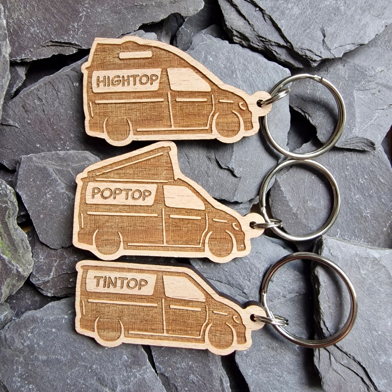 May include: Three wooden keychains shaped like vans with pop-top roofs. The keychains are labeled "Hightop", "Poptop", and "Tintop".