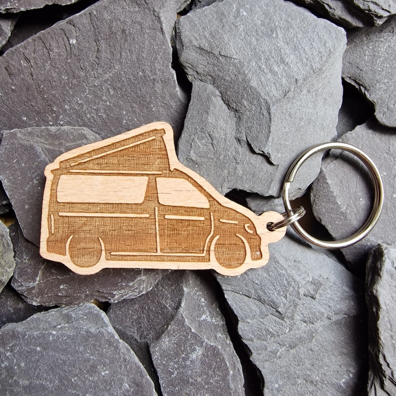 May include: A wooden keychain shaped like a camper van with a pop-up top. The keychain is attached to a silver metal key ring.