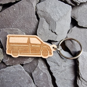 May include: Wooden keychain shaped like a van with a silver key ring. The keychain is light brown and has a detailed outline of a van.