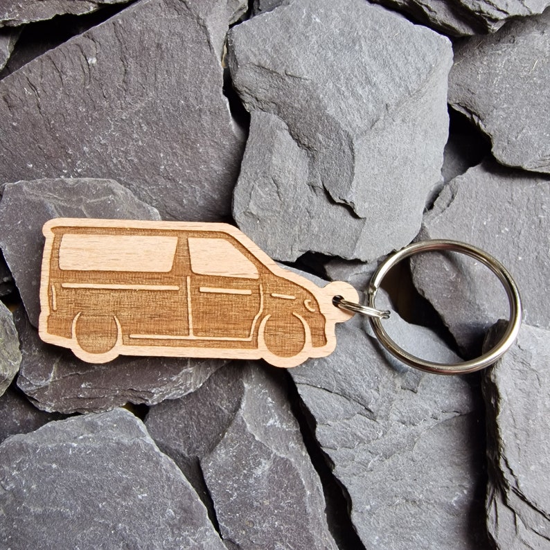 May include: Wooden keychain shaped like a van with a silver key ring. The keychain is light brown and has a detailed outline of a van.