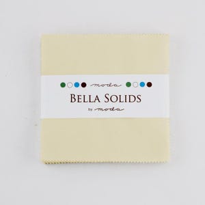 May include: A stack of square fabric pieces in a pale yellow color, wrapped with a white label. The label reads "BELLA SOLIDS" in a bold font, with the "moda" brand name above and below the text. The fabric edges have a scalloped trim.