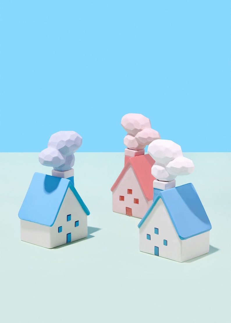 May include: A group of small, colourful houses with blue, pink, and white roofs and chimneys. The houses have square windows and are set against a light blue and green backdrop. The chimneys are topped with cloud-shaped details.