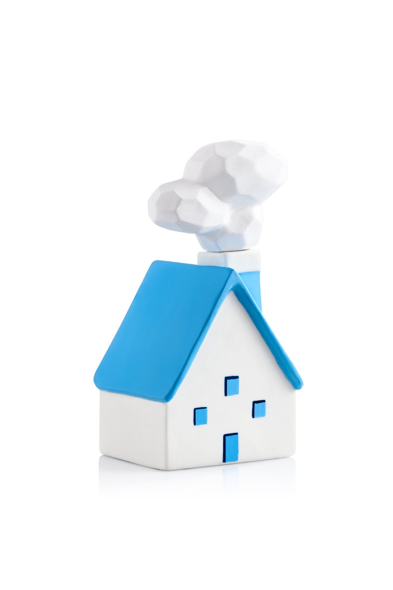 May include: A white ceramic house ornament with a blue roof and chimney, and a cloud-shaped smoke plume. The house has four blue square windows and a blue door. The ornament is on a white background.