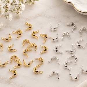 Peut inclure: Une collection de petits apprêts métalliques pour bijoux, appelés cache-nœuds ou perles à écraser. L'ensemble comprend des pièces dorées et argentées, chacune présentant une forme arrondie en coupelle avec une petite boucle de fixation.