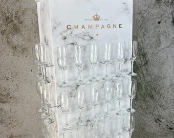 May include: A white marble champagne cart with a gold crown logo and the text "FONDEE EN 1743 CHAMPAGNE". The cart has four wheels and holds multiple champagne glasses.
