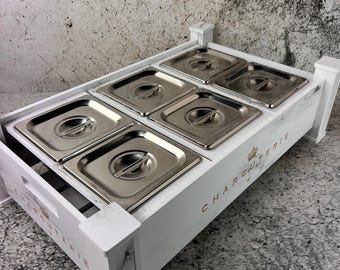 May include: White charcuterie serving tray with six stainless steel food containers. The tray has a marble-like design and the word "CHARCUTERIE" is printed on the side in gold lettering. A crown graphic is also visible.