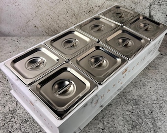 May include: A white charcuterie board with a marble design, featuring eight stainless steel containers with lids. The word "CHARCUTERIE" is printed on the side of the board.