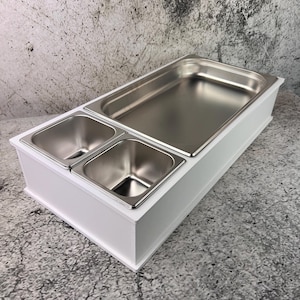 Op de afbeelding: Een witte houten serveerschaal met drie roestvrijstalen bakken. De bakken zijn rechthoekig en hebben een glanzend, reflecterend oppervlak. De schaal is ontworpen voor de horeca.