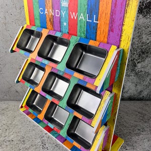 May include: A multi-coloured candy display stand with the text "CANDY WALL" and a crown logo. It features several stainless steel containers set against a backdrop of vertical, multi-coloured wooden planks. The stand is approximately 61 cm tall.