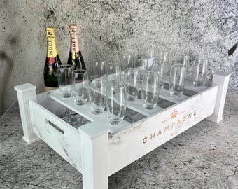 May include: White marble-patterned champagne crate with a gold logo that says "Champagne" and a crown. The crate has 12 slots for champagne glasses and two bottles of Moët & Chandon champagne.