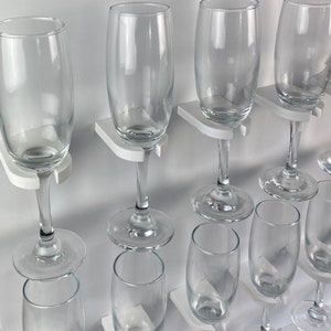 May include: A white wall-mounted wine glass rack with multiple clear glass wine glasses hanging from it.