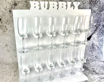 Puede incluir: Portavasos de champán de madera blanca con la palabra "Bubbly" en letras blancas en negrita. El portavasos tiene 15 ranuras para vasos de champán.