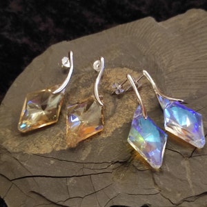 Könnte beinhalten: Ein Paar silberne Ohrringe mit einem diamantförmigen Kristall. Ein Ohrring hat einen klaren Kristall mit schillernden Regenbogenfarben, der andere Ohrring hat einen hellbernsteinfarbenen Kristall.