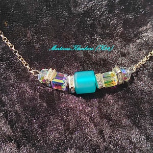 Puede incluir: Un collar de cadena de plata con una cuenta de vidrio azul turquesa y cuentas de cristal iridiscentes.