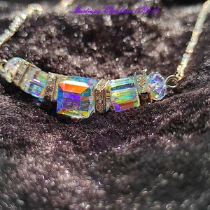 May include: A silver chain necklace with a rainbow iridescent crystal pendant. The pendant is made up of several smaller crystals that are arranged in a geometric pattern.