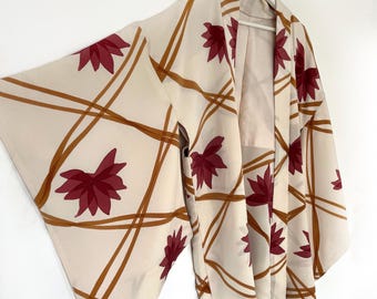 Puede incluir: Un kimono de color crema con un patrón geométrico de líneas marrones y diseños de flores rojas.