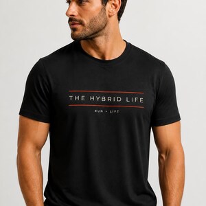May include: A black short-sleeved t-shirt featuring the white text THE HYBRID LIFE centred between two horizontal orange lines, with the words RUN • LIFT printed in smaller white text directly below the lines on the chest area.