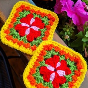 May include: Two crocheted squares with a flower design in the center. The flowers are red with white and pink accents. The squares are yellow, orange, green, and red.