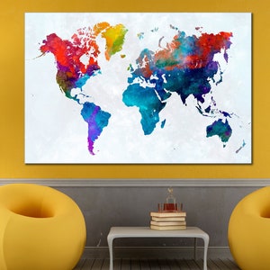 May include: A large, rectangular canvas print of a watercolor world map. The map features vibrant colors including red, blue, green, and yellow. The artwork is displayed on a yellow wall above a white table and two yellow beanbag chairs.