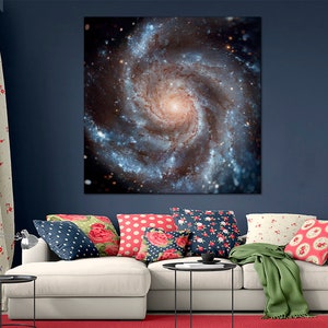Op de afbeelding: Een witte bank met kleurrijke kussens in een woonkamer. Een groot canvas print van een draaiende galaxie hangt aan de muur achter de bank.