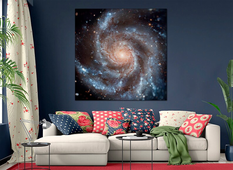 Op de afbeelding: Een witte bank met kleurrijke kussens in een woonkamer. Een groot canvas print van een draaiende galaxie hangt aan de muur achter de bank.
