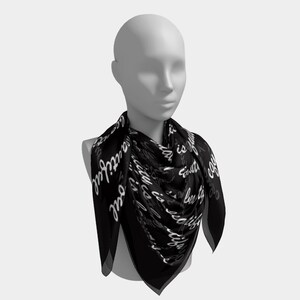 May include: A black square scarf with white cursive text that reads "Beauty is in the soul". The scarf is draped around a mannequin's neck, showcasing its design and shape. The scarf is made of a lightweight material.