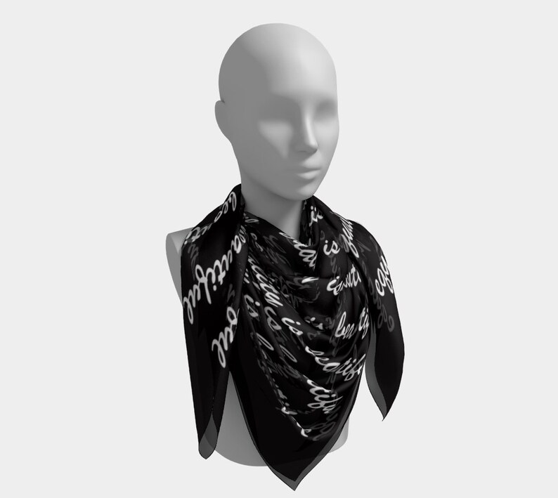 May include: A black square scarf with white cursive text that reads "Beauty is in the soul". The scarf is draped around a mannequin's neck, showcasing its design and shape. The scarf is made of a lightweight material.
