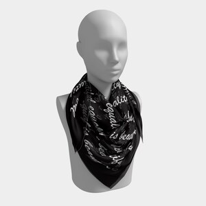 May include: A black square scarf with the words "equality is beautiful" in white cursive script. The scarf is draped around a mannequin's neck, showcasing the design and fabric.