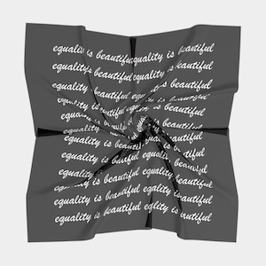 May include: A dark gray square scarf with the words "equality is beautiful" repeated in white script across the fabric. The scarf is twisted and folded, creating a dynamic visual effect.