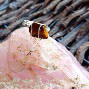 May include: A silver wire wrapped ring with a brown tiger's eye stone. The ring is sitting on a pink rose quartz.