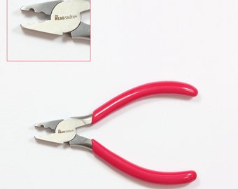 Puede incluir: Un par de alicates con mangos rojos y mordazas plateadas. Las mordazas están diseñadas para crimpado y tienen una pequeña abertura. Los alicates están etiquetados como "The Beadsmith".
