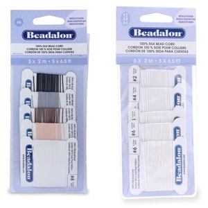 Può includere: Due confezioni di cordoncino per perline Beadalon 100% seta. La confezione a sinistra contiene cinque bobine di cordoncino di diversi colori: nero, grigio, marrone, beige e bianco. La confezione a destra contiene cinque bobine di cordoncino bianco. Ogni bobina è etichettata con la dimensione del cordoncino: #2, #4 e #6. Entrambe le confezioni sono etichettate con il logo Beadalon e il testo "100% Silk Bead Cord".