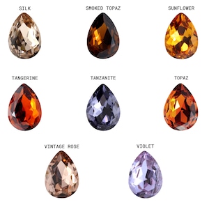 May include: Nine teardrop-shaped glass beads in various colors, including tan, orange, brown, purple, and blue. The beads are arranged in three rows of three, with each bead labeled with a color name.