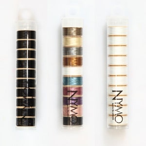 May include: Three clear plastic tubes containing spools of thread. The tubes are labelled "NYMO" and "By the Beadsmith". The spools of thread are in various colours, including black, white, brown, gold, silver, blue, pink, and purple.