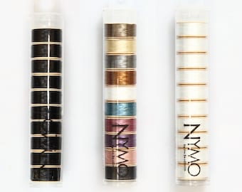 May include: Three clear plastic tubes containing spools of thread. The tubes are labeled "NYMO" and "By the Beadsmith". The spools of thread are in various colors, including black, white, brown, gold, silver, blue, pink, and purple.