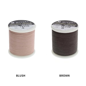 Op de afbeelding: Twee spoelen Miyuki Beading Thread, &eacute;&eacute;n in blush roze en &eacute;&eacute;n in bruin. De spoelen zijn gelabeld met de merknaam, het type draad, dtex, lotnummer en kleurnummer.