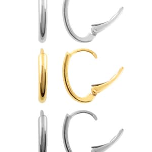 May include: A set of three hoop earrings in silver and gold. The earrings are all the same size and shape, but they are different colours. The earrings are made of metal and have a hinged clasp.