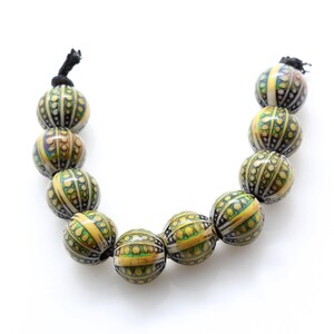 Puede incluir: Una hebra de cuentas con patrones amarillos, verdes y negros. Las cuentas son redondas y tienen una superficie texturizada.