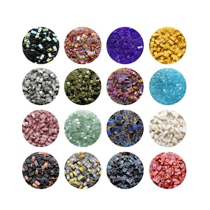 Op de afbeelding: Een verzameling kleurrijke rocailles in verschillende tinten, waaronder zwart, iriserend, paars, geel, zilver, olijfgroen, roze en blauw. De kralen zijn in cirkelvormige patronen gerangschikt, waarbij hun rechthoekige vorm en iriserende afwerking worden benadrukt. Ideaal voor het maken van sieraden.