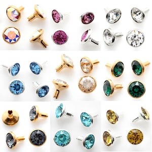 May include: A collection of round crystal rivets in various colors including clear, pink, blue, green, yellow, and grey. Each rivet features a faceted gemstone set in a metal base with a pronged back for attachment to fabric or leather materials.