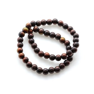 May include: A brown wooden beaded bracelet with a dark brown color. The bracelet is made of round beads and is stacked on top of itself.