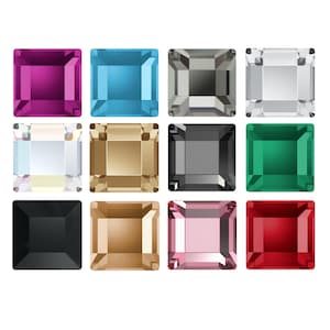 Può includere: Una collezione di dodici cristalli sfaccettati di forma quadrata disposti in una griglia. I colori includono magenta, blu brillante, argento, trasparente, iridescente, oro, grigio scuro, verde smeraldo, nero, marrone chiaro, rosa tenue e rosso intenso.