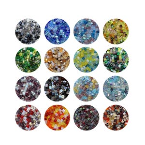 Op de afbeelding: Een verzameling van zestien cirkelvormige arrangementen van kleine, vierkante glazen kralen in verschillende kleuren. De kralen zijn in tinten blauw, groen, geel, rood en zwart, met enkele iriserende en metallic afwerkingen. Ideaal voor het maken van sieraden en knutselen.