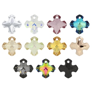 Puede incluir: Una colección de once colgantes de cristal en forma de cruz dispuestos en tres filas. Los colgantes presentan varios colores, incluyendo transparente, iridiscente, rosa, azul, oro, amarillo, metálico, gris, multicolor y negro, cada uno con un orificio.