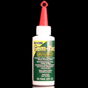 May include: A white bottle of Beacon Gem-Tac permanent glue with a red cap. The bottle is labeled with the product name, instructions for use, and a warning that it is non-toxic. The bottle contains 59.15 ml (2 fl oz) of glue.