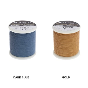 Op de afbeelding: Twee spoelen Miyuki Beading Thread, &eacute;&eacute;n donkerblauw en &eacute;&eacute;n goud. De spoelen zijn gelabeld met de merknaam, het type draad, de maat, het lotnummer en de kleurcode.